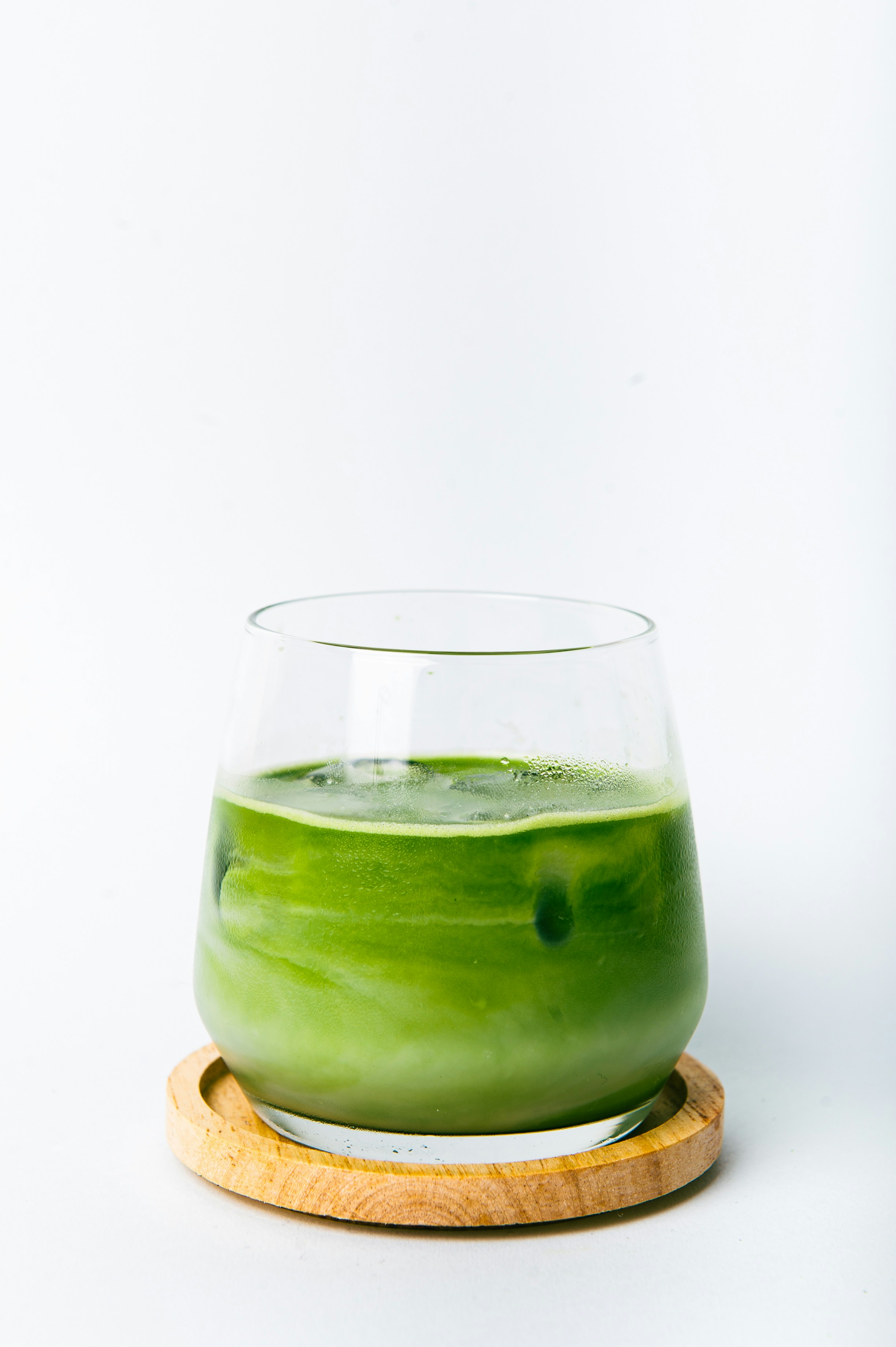 A tall glass of plain iced matcha on a minimal white background