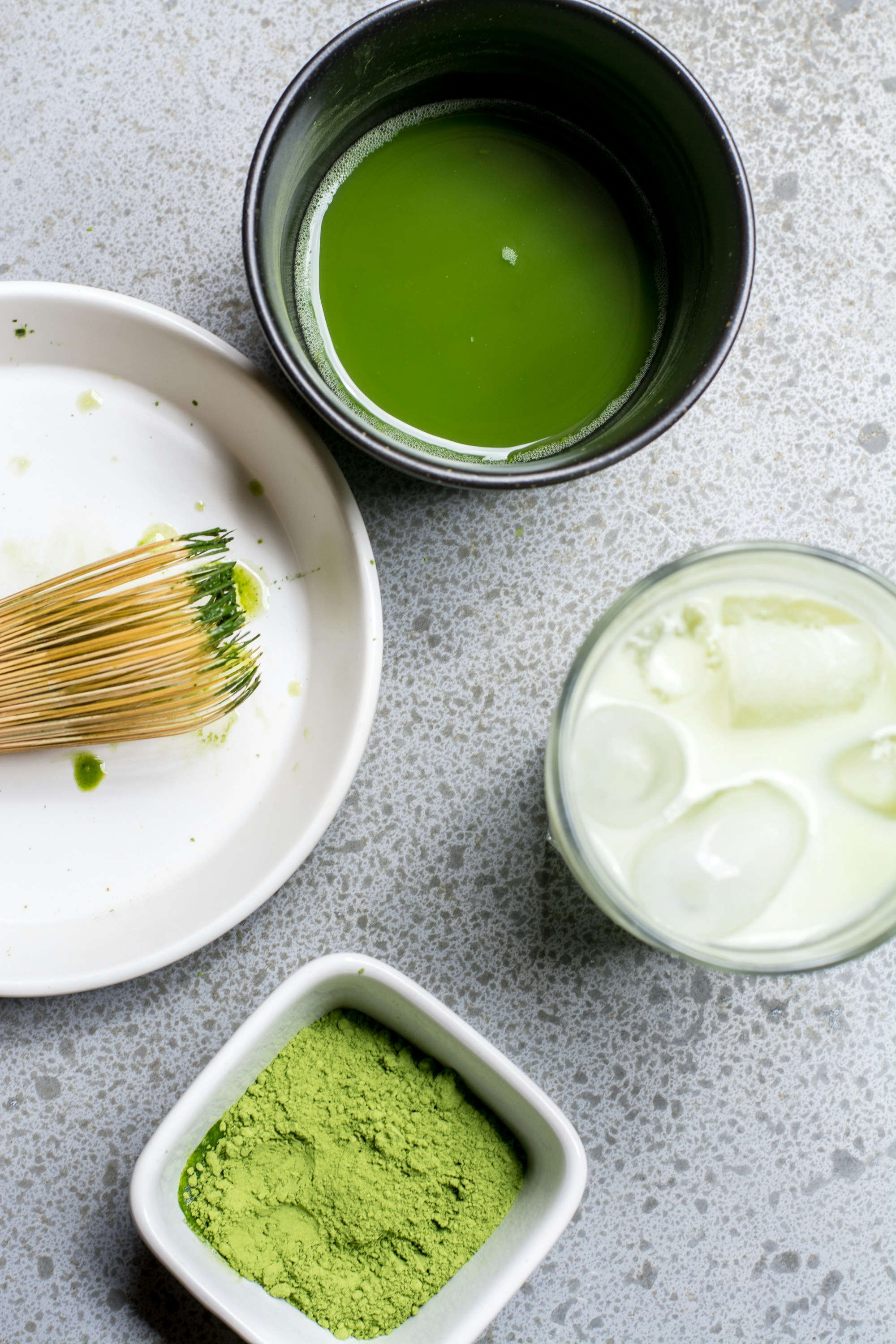 Flatlay of matcha powder and whole tea leaves arranged with traditional tools