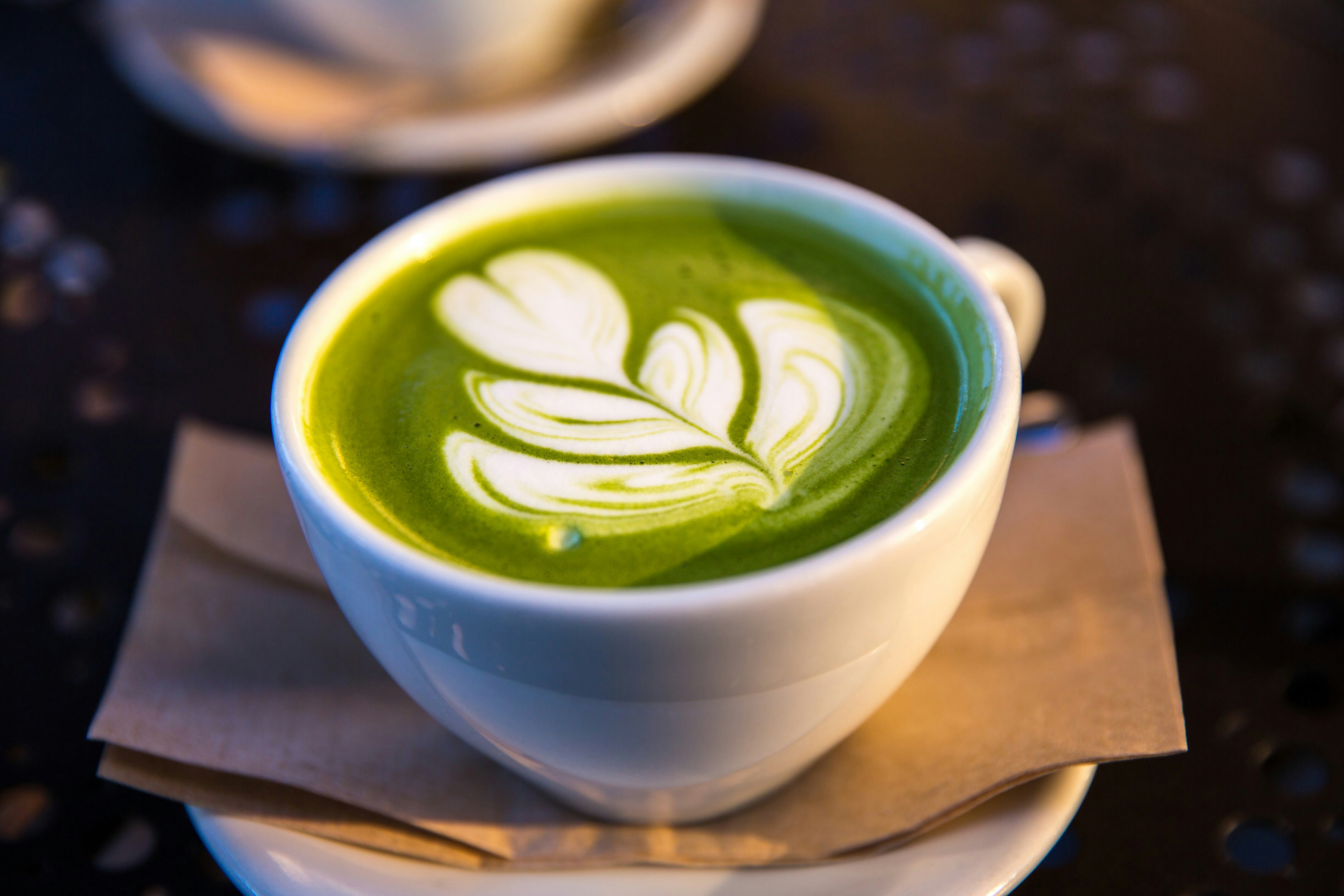 Matcha latte art with a delicate leaf pattern on dark ceramic